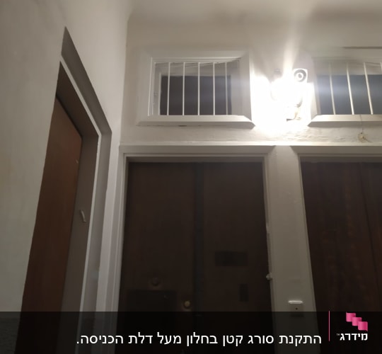 חלון עם סורגים מעל דלת כניסה מוארת